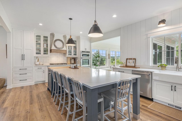 8608 52nd St SE, Ada, MI 49301 - kitchen with stainless steel appliances, white cabinets, a breakfast bar, light wood-type flooring, and decorative backsplash