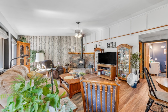 76 Meceola Ct, Hersey, MI 49639 - living room featuring wallpapered walls, wood finished floors, a wood stove, a ceiling fan, and an accent wall