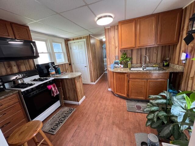 1325 Maude Ave NE, Grand Rapids, MI 49505 - kitchen with black microwave, gas range gas stove, light wood-style floors, brown cabinets, and wooden walls