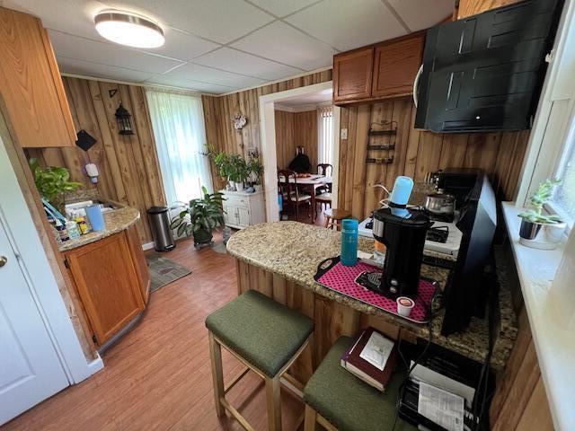 1325 Maude Ave NE, Grand Rapids, MI 49505 - kitchen featuring brown cabinetry, wooden walls, light wood-style flooring, a kitchen breakfast bar, and a paneled ceiling