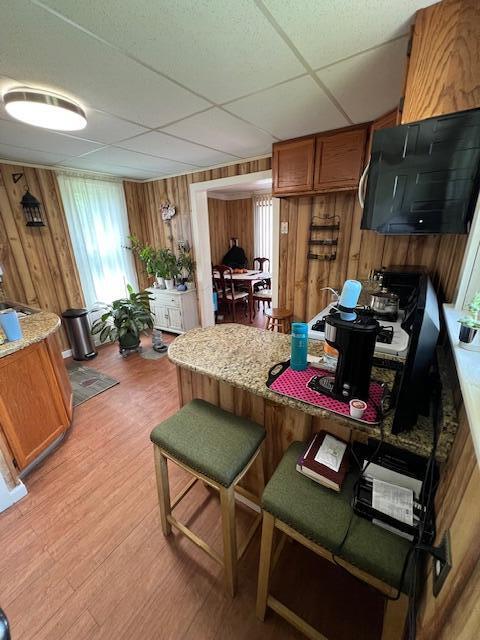 1325 Maude Ave NE, Grand Rapids, MI 49505 - kitchen featuring brown cabinets, a paneled ceiling, wooden walls, light wood finished floors, and a kitchen bar