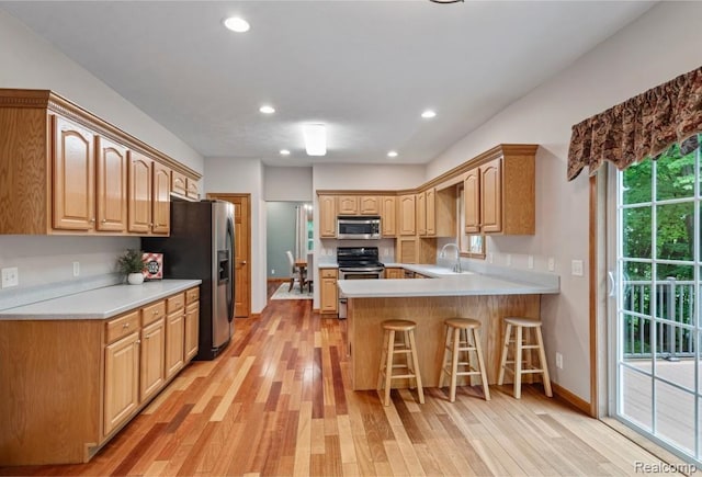 12151 Vergennes St, Lowell, MI 49331 - kitchen with stainless steel appliances, a peninsula, light wood-style floors, a breakfast bar area, and light countertops