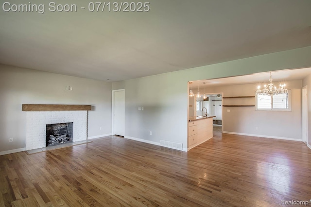 7709 Shelley Dr, Clarkston, MI 48348 - unfurnished living room featuring a chandelier, wood finished floors, and a brick fireplace