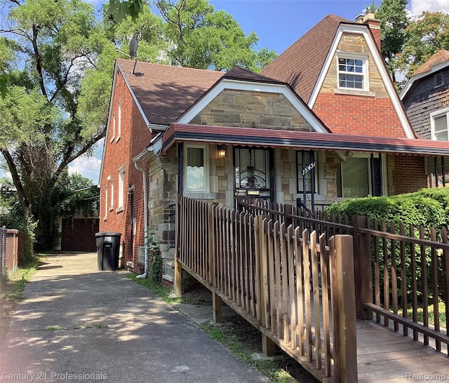 15451 Prest St, Detroit, MI 48227 - view of front of home featuring stone siding, covered porch, roof with shingles, and a chimney