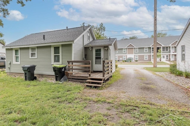 1312 Bayliss St, Midland, MI 48640 - back of property featuring a deck, roof with shingles, gravel driveway, and a lawn