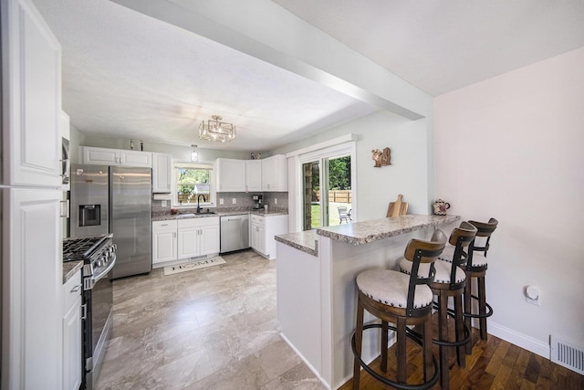 119 Burt Ave, Jackson, MI 49201 - kitchen with appliances with stainless steel finishes, a peninsula, a kitchen breakfast bar, white cabinets, and decorative backsplash