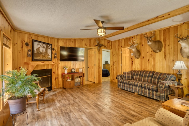 13113 Pinewood St NE, Gowen, MI 49326 - living room with ceiling fan, a textured ceiling, wooden walls, wood finished floors, and a fireplace with flush hearth