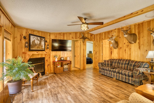 13113 Pinewood St NE, Gowen, MI 49326 - living room with a ceiling fan, a textured ceiling, wooden walls, wood finished floors, and a fireplace with flush hearth