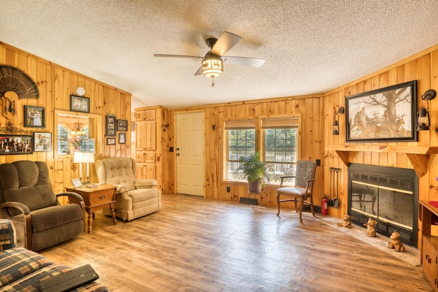 13113 Pinewood St NE, Gowen, MI 49326 - living area featuring wood walls, a fireplace with flush hearth, a ceiling fan, a textured ceiling, and wood finished floors