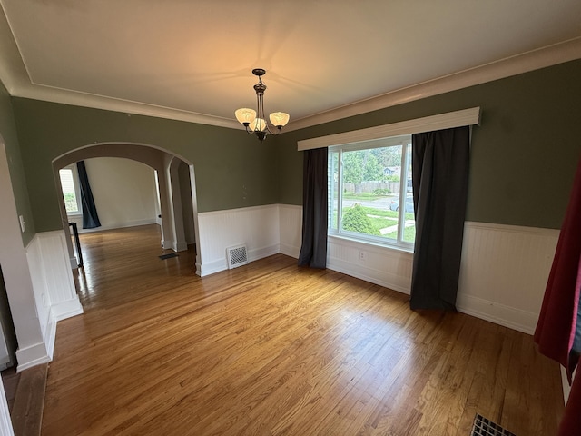 1316 Vassar Dr, Kalamazoo, MI 49001 - spare room featuring arched walkways, a chandelier, a wainscoted wall, wood finished floors, and plenty of natural light