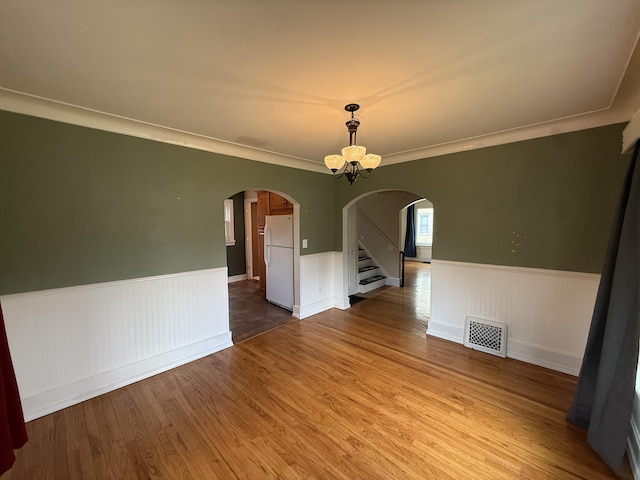 1316 Vassar Dr, Kalamazoo, MI 49001 - empty room featuring arched walkways, a wainscoted wall, wood finished floors, crown molding, and stairway