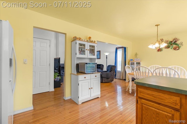 3070 10th St, Monroe, MI 48162 - kitchen featuring white refrigerator with ice dispenser, a chandelier, light wood-type flooring, glass insert cabinets, and pendant lighting