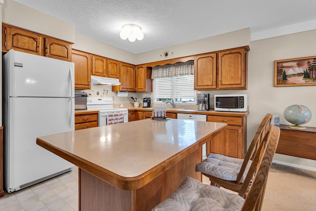 263 Westshore Dr, Jerome, MI 49249 - kitchen with white appliances, under cabinet range hood, brown cabinetry, a breakfast bar, and a textured ceiling