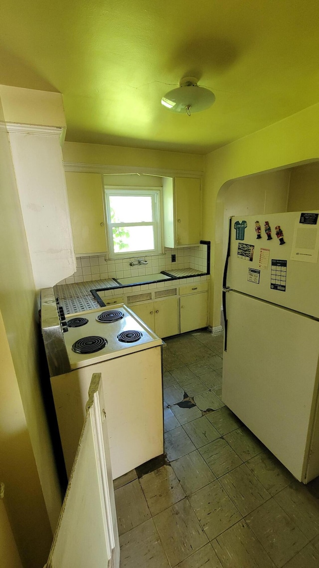 1109 Meadowbrooke St, Inkster, MI 48141 - kitchen featuring freestanding refrigerator, white cabinetry, decorative backsplash, arched walkways, and light countertops