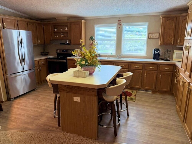 7878 Schooner Ln, Canadian Lakes, MI 49346 - kitchen with stainless steel appliances, crown molding, a kitchen bar, a textured ceiling, and light wood-style flooring