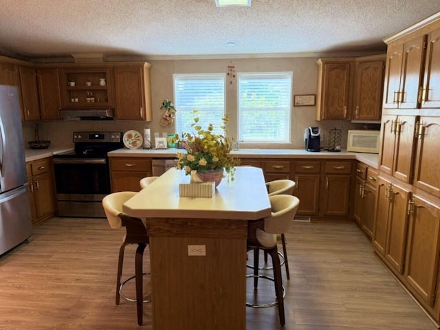 7878 Schooner Ln, Canadian Lakes, MI 49346 - kitchen with appliances with stainless steel finishes, under cabinet range hood, a kitchen bar, light wood-style flooring, and a textured ceiling