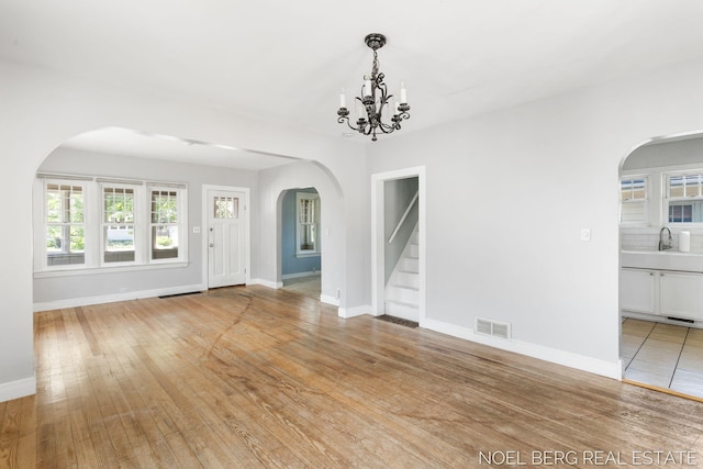 1307 Waverly Ave, Grand Haven, MI 49417 - unfurnished room featuring arched walkways, stairway, light wood-style flooring, and a chandelier