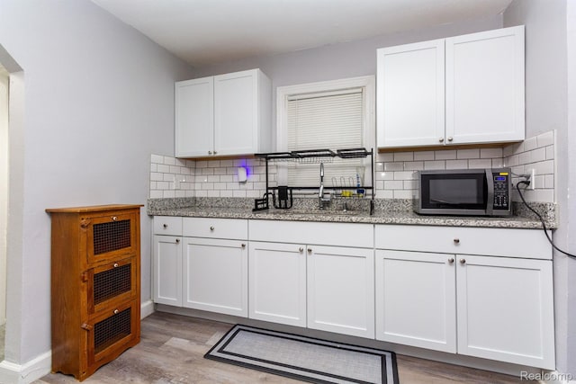 3602 Chatsworth St, Detroit, MI 48224 - kitchen featuring stainless steel microwave, light wood-style floors, backsplash, white cabinets, and light stone counters