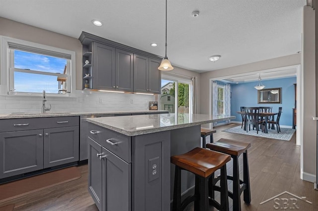 936 Appaloosa Pass, Auburn, MI 48611 - kitchen featuring gray cabinetry, a kitchen bar, decorative backsplash, a kitchen island, and hanging light fixtures