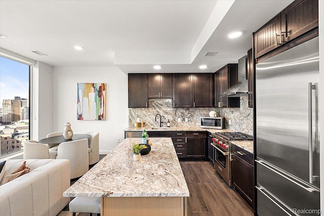 330 Gratiot Ave Unit 1504, Detroit, MI 48226 - kitchen featuring high quality appliances, wall chimney range hood, dark wood-type flooring, backsplash, and dark brown cabinetry