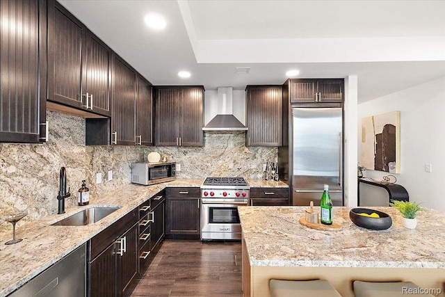 330 Gratiot Ave Unit 1504, Detroit, MI 48226 - kitchen with high quality appliances, wall chimney exhaust hood, dark brown cabinetry, light stone counters, and dark wood finished floors