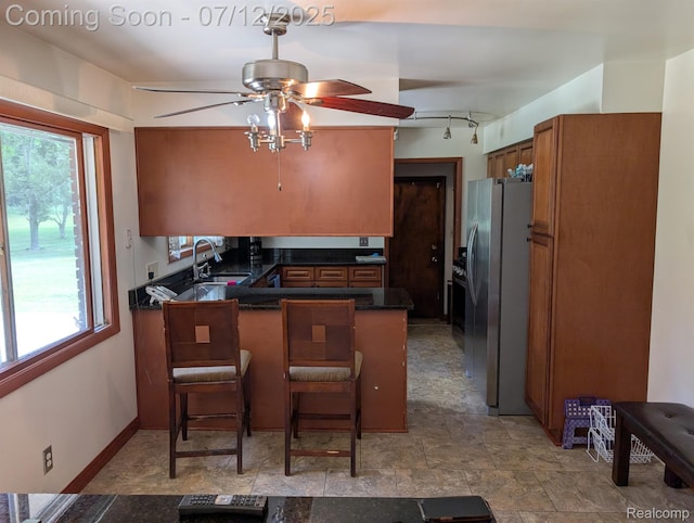 22048 Rougewood Dr, Southfield, MI 48033 - kitchen with freestanding refrigerator, ceiling fan, a peninsula, brown cabinetry, and a breakfast bar