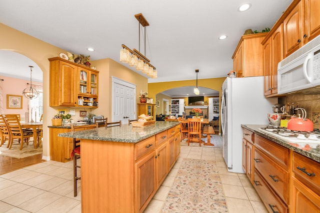 9095 Marsh Cir, Galesburg, MI 49053 - kitchen featuring arched walkways, white appliances, a kitchen island, dark stone counters, and recessed lighting