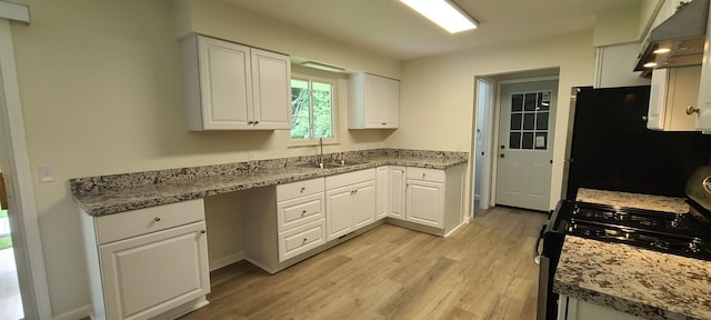 4404 Eastport Dr, Bridgeport, MI 48722 - kitchen with black gas stove, under cabinet range hood, freestanding refrigerator, white cabinetry, and light wood-style floors