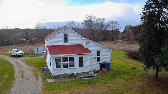 524 S Cherry St, Evart, MI 49631 - rear view of house featuring driveway, a yard, a storage unit, roof with shingles, and a wooded view