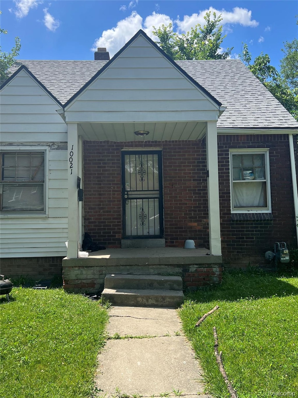 10021 Coyle St, Detroit, MI 48227 - bungalow-style home featuring covered porch, brick siding, roof with shingles, a chimney, and a front lawn