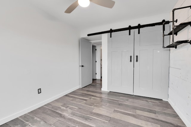 221 Pinewood Cir, Plymouth, MI 48170 - unfurnished bedroom with a barn door, wood finished floors, and a ceiling fan
