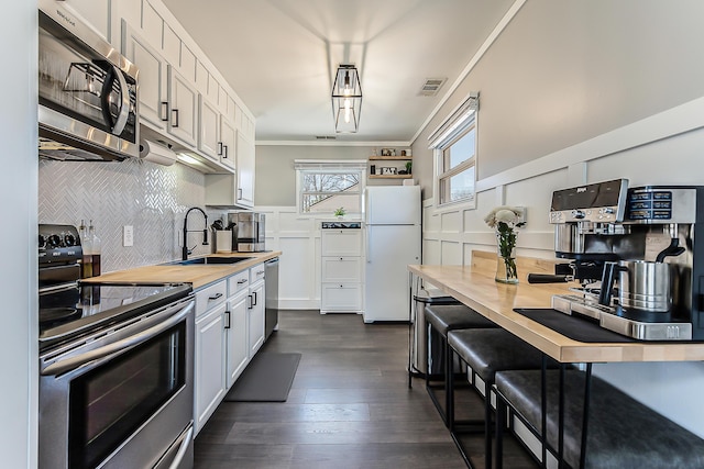 405 Spring St, Saline, MI 48176 - kitchen featuring stainless steel appliances, ornamental molding, dark wood-type flooring, white cabinetry, and decorative backsplash