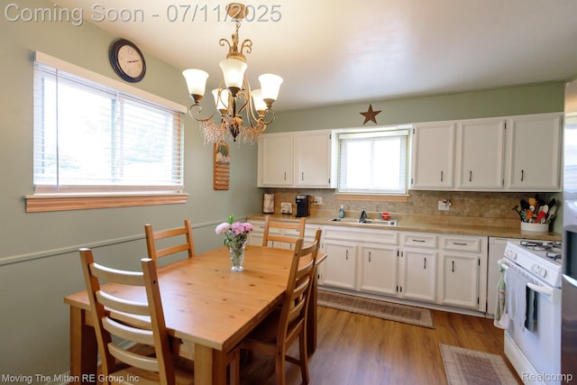 13620 Aston St, Romulus, MI 48174 - kitchen with white gas range oven, light wood finished floors, white cabinets, backsplash, and a chandelier
