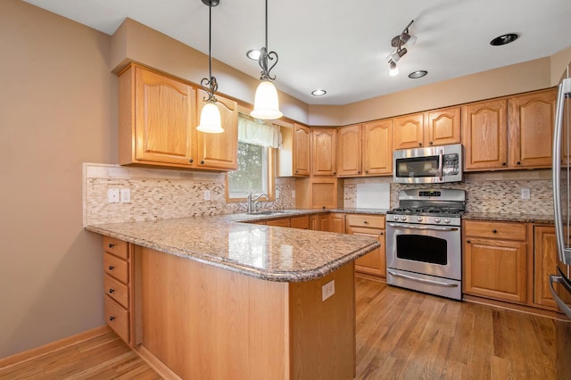 4291 Bramblewood Ct, Dorr, MI 49323 - kitchen with appliances with stainless steel finishes, light wood finished floors, a peninsula, tasteful backsplash, and hanging light fixtures