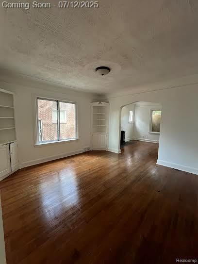 15475 Prest St, Detroit, MI 48227 - unfurnished living room featuring arched walkways, dark wood finished floors, a textured ceiling, and built in shelves