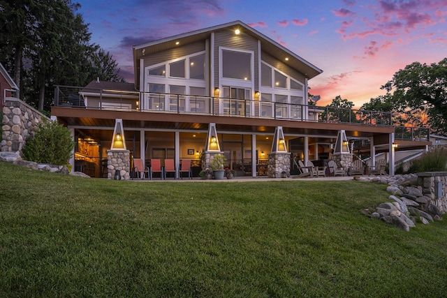 481 Seminole Rd, Norton Shores, MI 49444 - back of property at dusk featuring a lawn, stone siding, and a patio