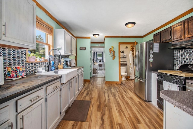 515 Locust St, Howard City, MI 49329 - kitchen featuring under cabinet range hood, black gas range oven, tasteful backsplash, light wood-style floors, and crown molding