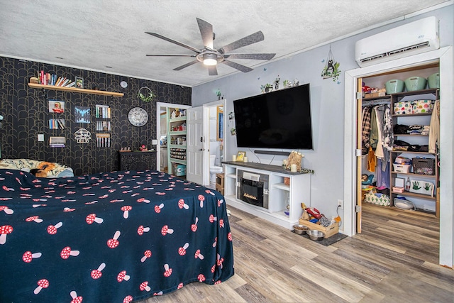 515 Locust St, Howard City, MI 49329 - bedroom featuring a wall mounted AC, a textured ceiling, wallpapered walls, wood finished floors, and a spacious closet