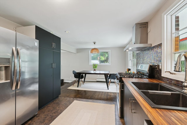2422 Essex, Ann Arbor, MI 48104 - kitchen featuring appliances with stainless steel finishes, wall chimney exhaust hood, backsplash, wooden counters, and hanging light fixtures
