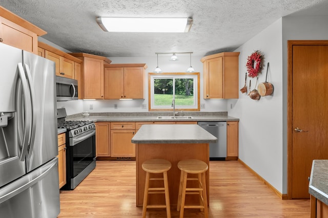 22100 N Uldriks Dr, Battle Creek, MI 49017 - kitchen with appliances with stainless steel finishes, light wood-style flooring, a kitchen island, a breakfast bar area, and a textured ceiling