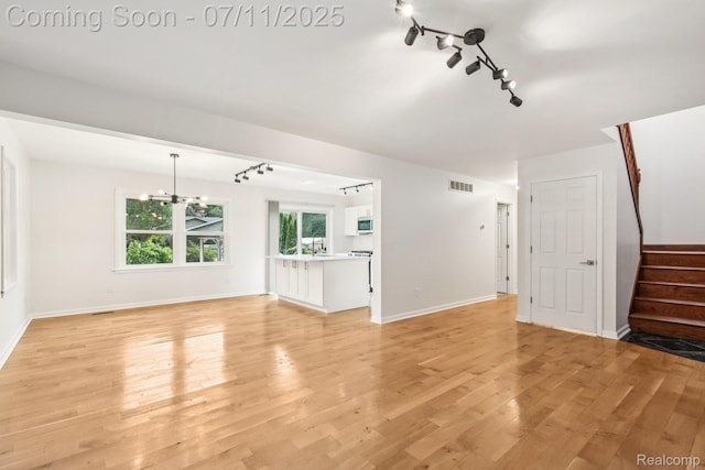 10746 Winthrop, Pinckney, MI 48169 - unfurnished living room with rail lighting, stairway, light wood-style floors, and a chandelier