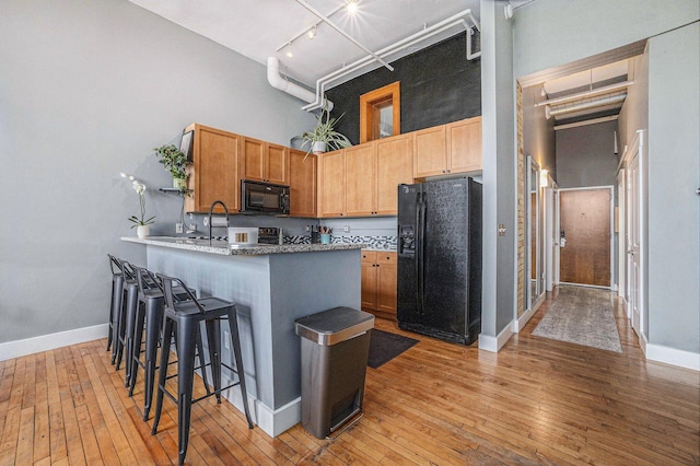 600 Broadway Ave NW Unit 402, Grand Rapids, MI 49504 - kitchen featuring black appliances, a towering ceiling, light wood-style floors, a kitchen breakfast bar, and a peninsula