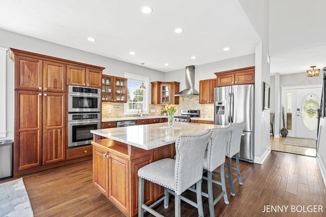 7066 Country Springs Dr SW, Byron Center, MI 49315 - kitchen with appliances with stainless steel finishes, wall chimney exhaust hood, a kitchen island, dark wood-type flooring, and glass insert cabinets