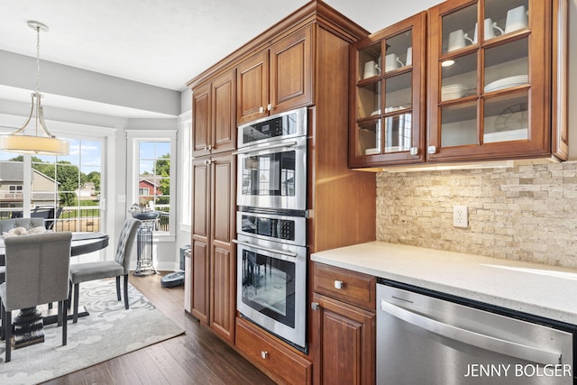 7066 Country Springs Dr SW, Byron Center, MI 49315 - kitchen with appliances with stainless steel finishes, brown cabinetry, glass insert cabinets, tasteful backsplash, and dark wood-style floors