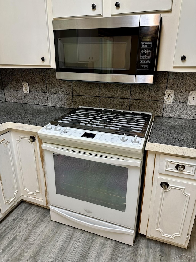 4650 Village Dr, Saginaw, MI 48638 - kitchen with white gas stove, stainless steel microwave, decorative backsplash, tile counters, and white cabinetry