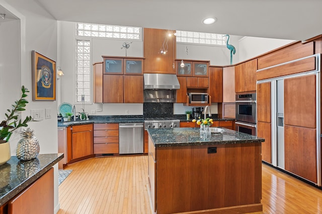 2323 Solano Dr, Wolverine Lake, MI 48390 - kitchen featuring stainless steel appliances, wall chimney range hood, light wood-style flooring, brown cabinets, and glass insert cabinets