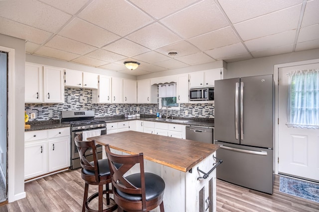 1051 Vallado Dr, Weidman, MI 48893 - kitchen featuring appliances with stainless steel finishes, a drop ceiling, light wood-style floors, white cabinetry, and decorative backsplash
