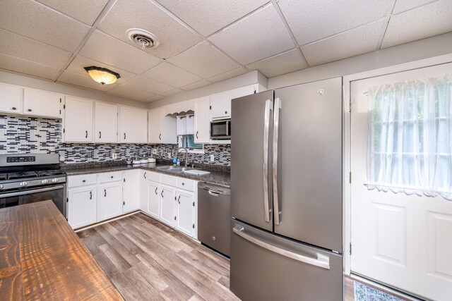 1051 Vallado Dr, Weidman, MI 48893 - kitchen featuring stainless steel appliances, a drop ceiling, light wood-style flooring, white cabinets, and decorative backsplash