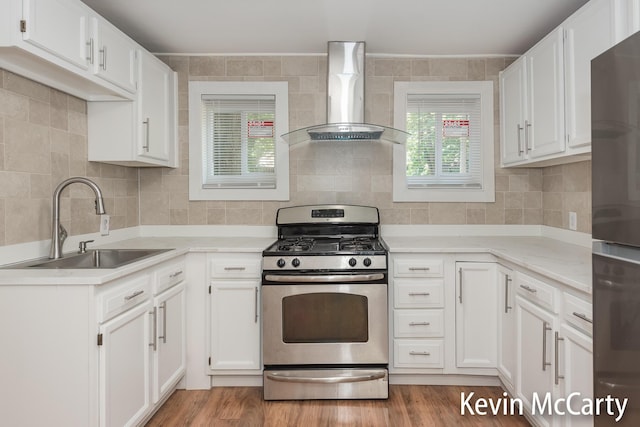 214 Bradford St NE, Grand Rapids, MI 49503 - kitchen with gas stove, wall chimney range hood, white cabinetry, and tasteful backsplash