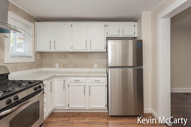 214 Bradford St NE, Grand Rapids, MI 49503 - kitchen with appliances with stainless steel finishes, wall chimney range hood, white cabinets, wood finished floors, and crown molding